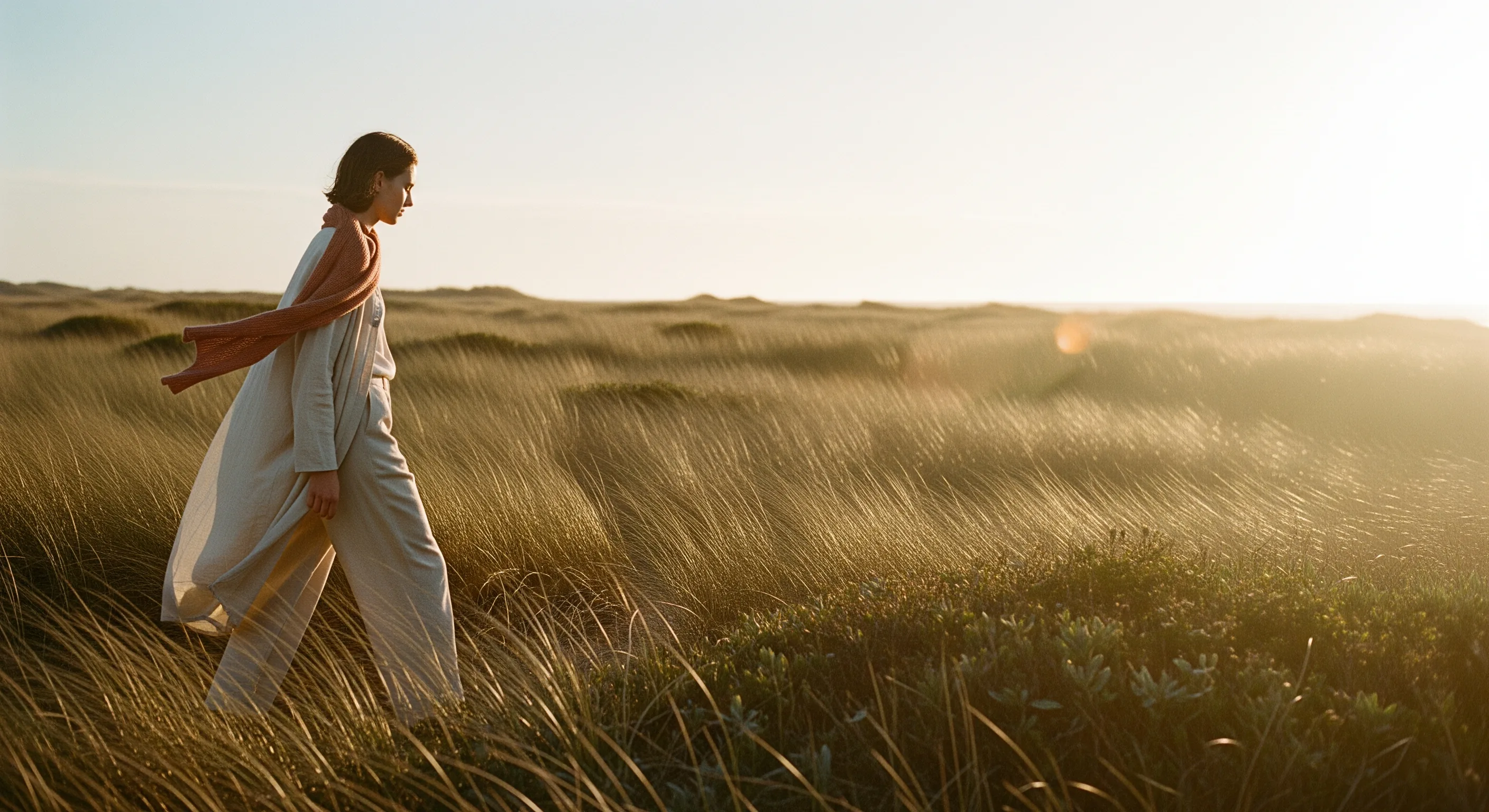 Summer 2026 campaign — figure walking through golden coastal grasses at sunset